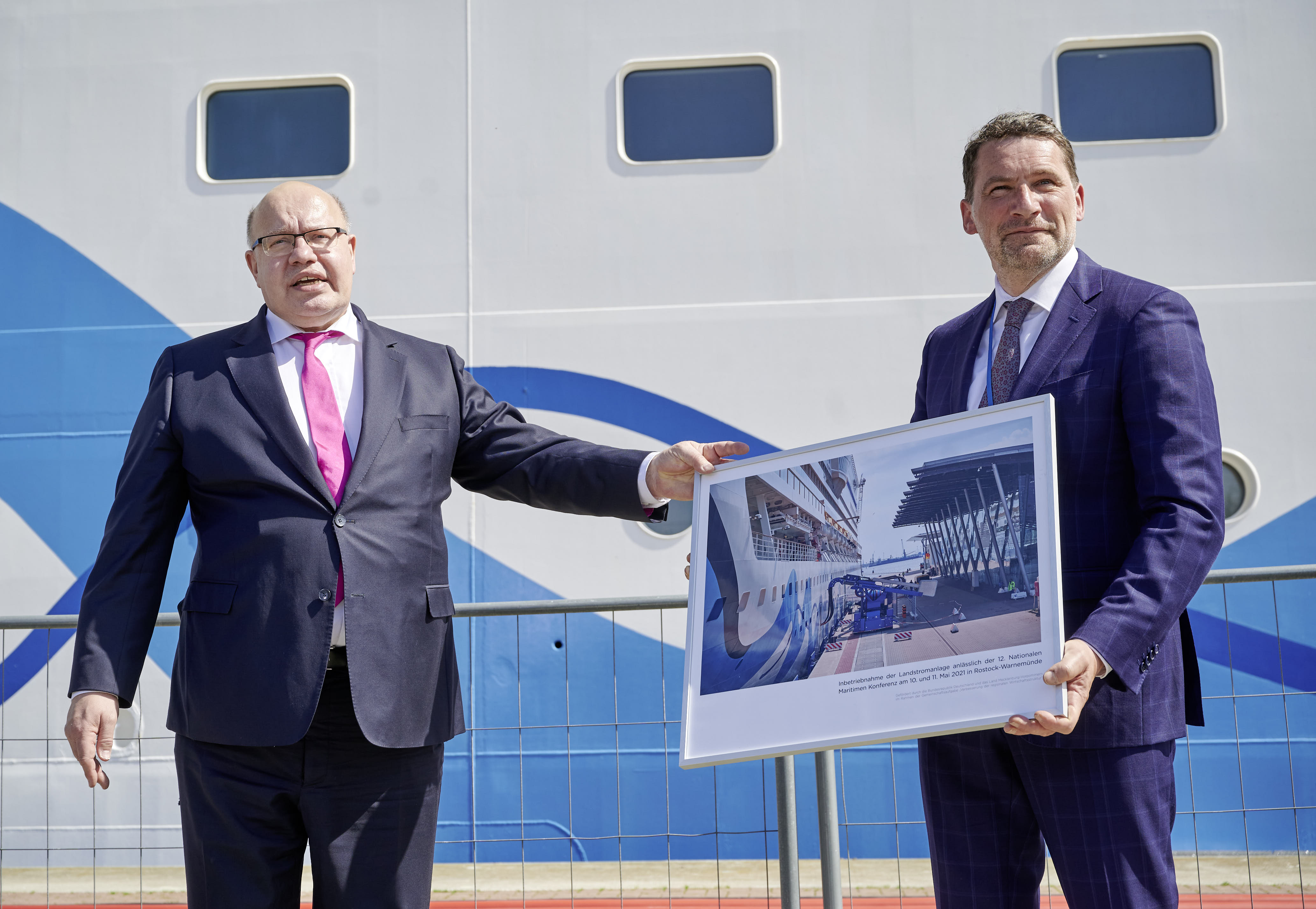 Bundeswirtschaftsminister Peter Altmaier und ROSTOCK PORT-Geschäftsführer Jens A. Scharner übergeben vor dem Kreuzfahrtschiff AIDAsol ein Bild der Landstromanlage