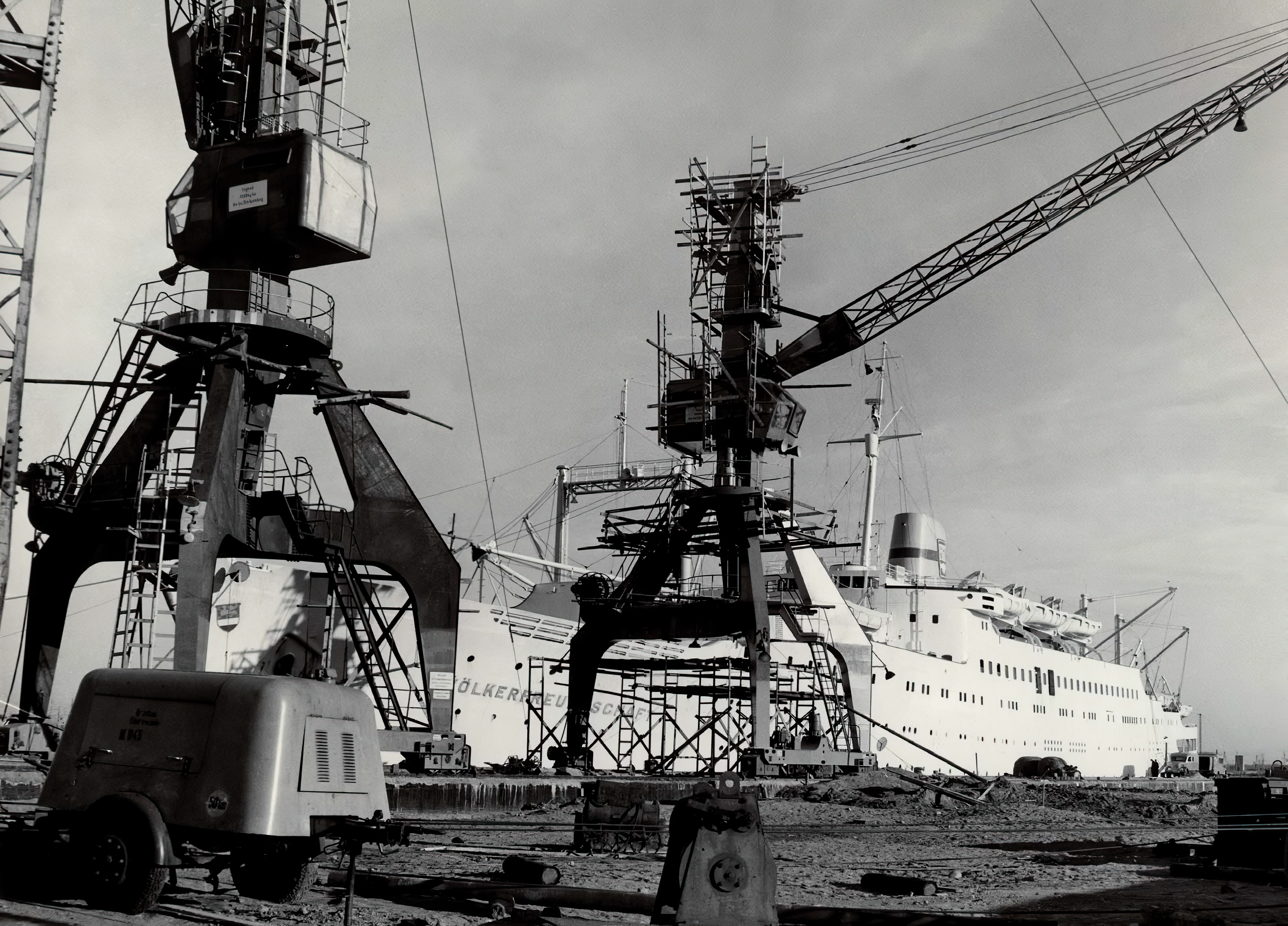 Historisches Schwarz-Weiß-Archivfoto: Das Schiff „Völkerfreundschaft“ im Hintergrund und zwei Hafenkräne im Vordergrund