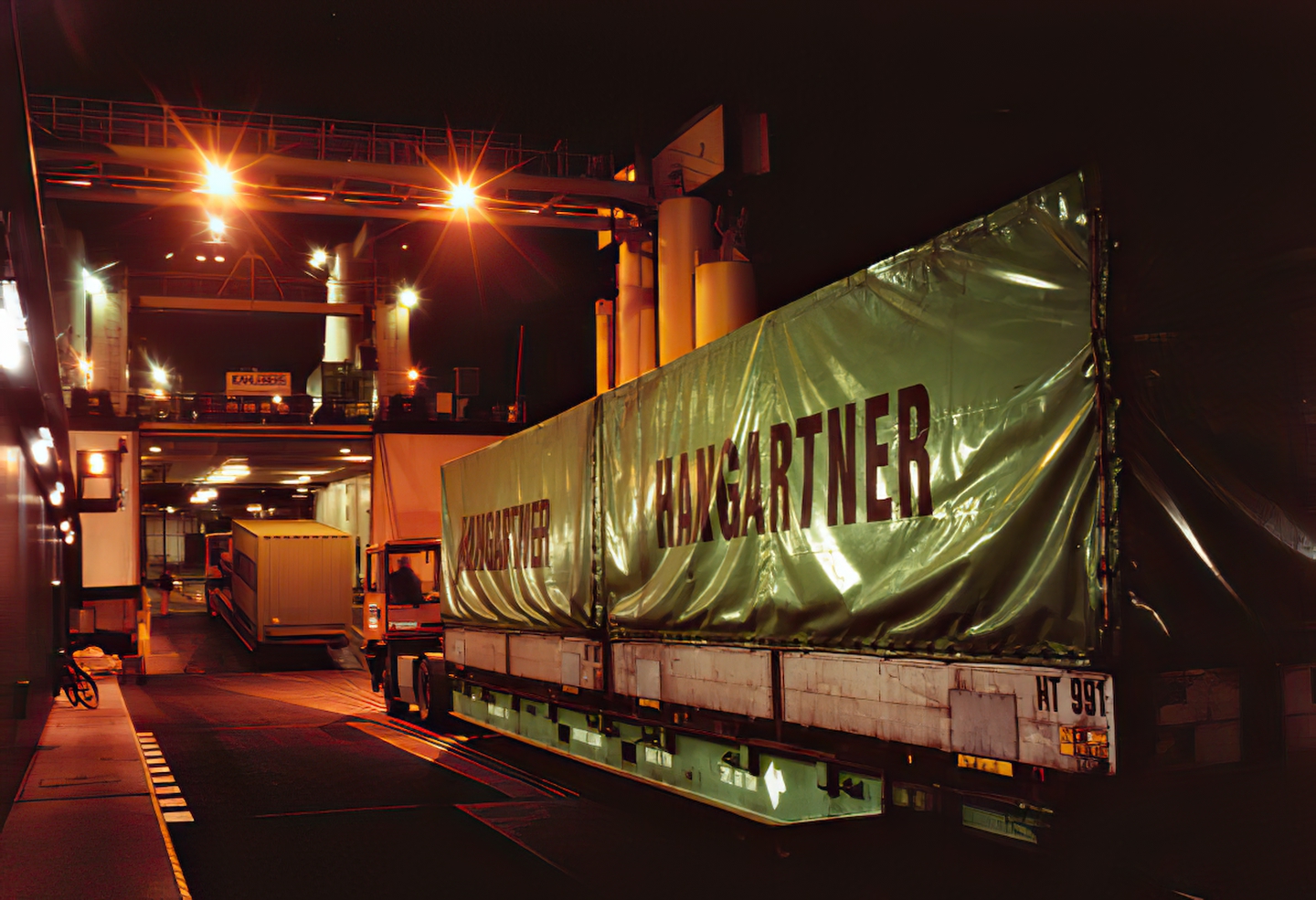 Historisches Archivfoto bei Nacht: Zwei Trailer werden unter Flutlichtbeleuchtung auf ein RoRo-Schiff verladen