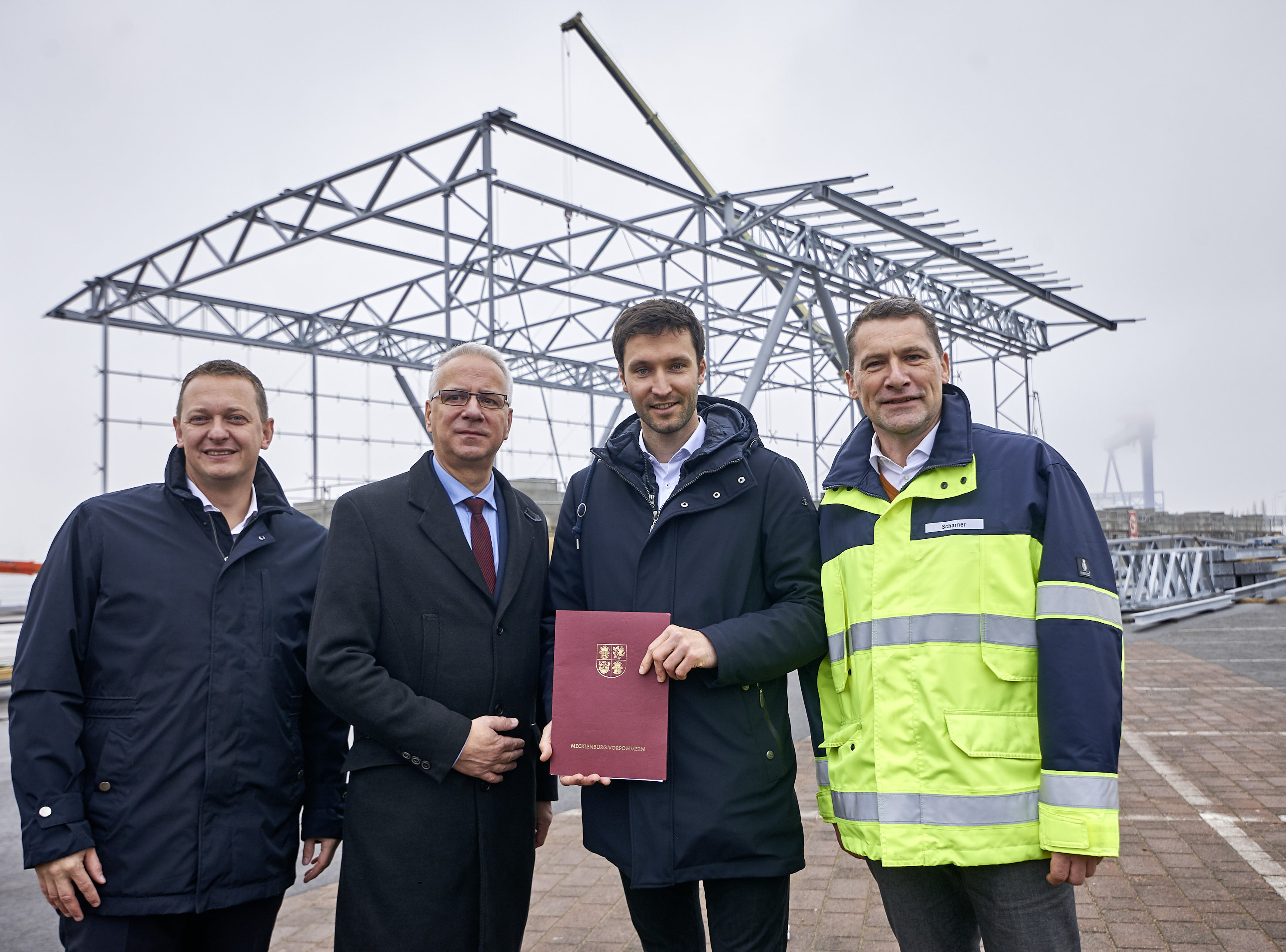 Vier Männer auf der Baustelle vor dem Hochbau des Kreuzfahrtterminals am Liegeplatz WCC 8.