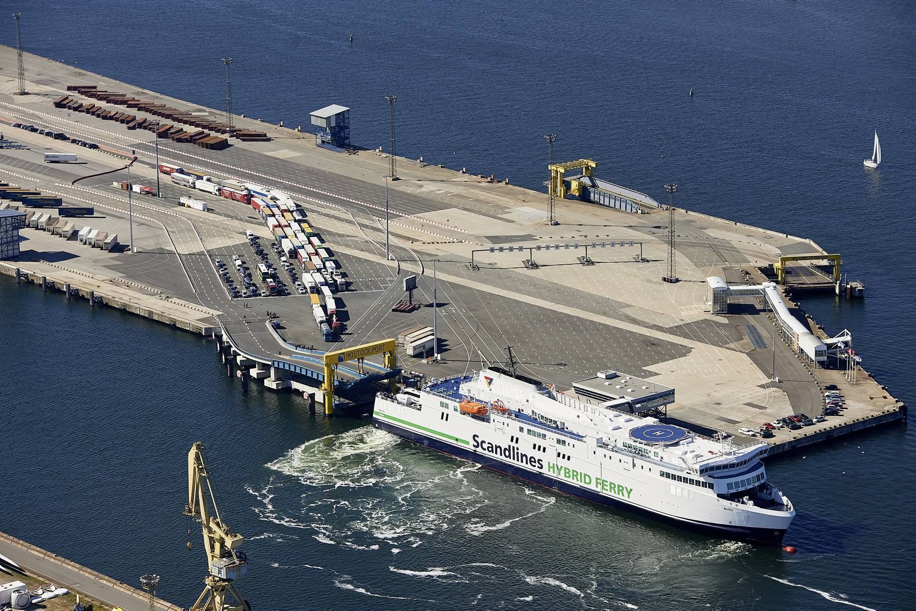 Luftbild des Fährterminals mit einer Scandlines-Fähre im Vordergrund sowie wartenden Lastwagen und Autos auf den Aufstellflächen.