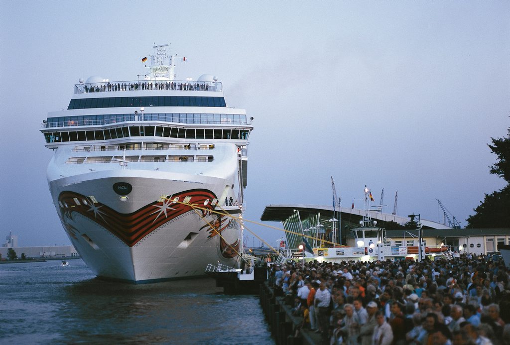 Cruise ship moored at berth P7. In the foreground, numerous people are standing and sitting on the pier, looking out over the water.