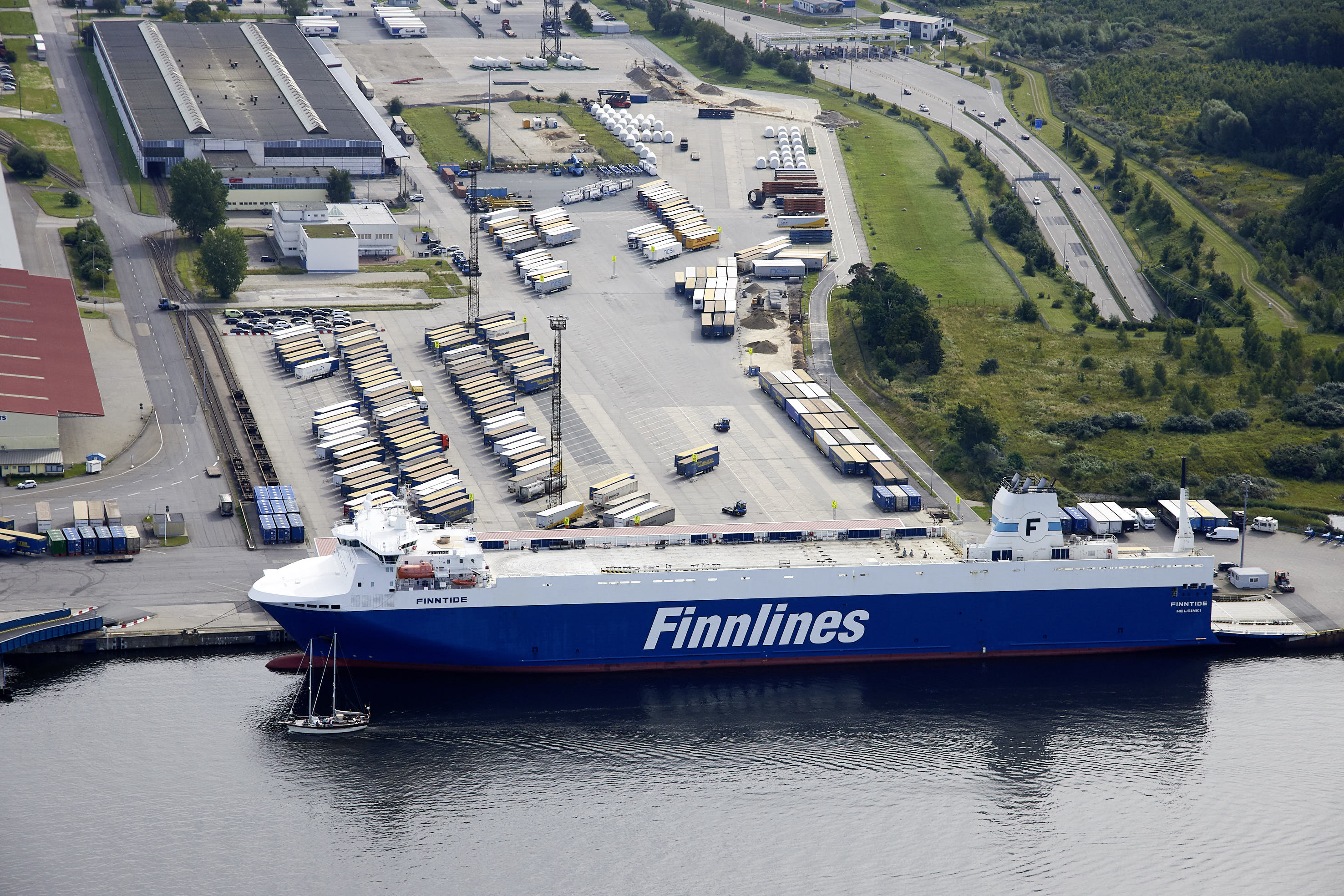 Luftaufnahme eines RoRo-Schiffs der Reederei Finnlines im Vordergrund. Im Hintergrund sind die Vorstellfläche und Kaihallen am Liegeplatz 60 zu sehen.
