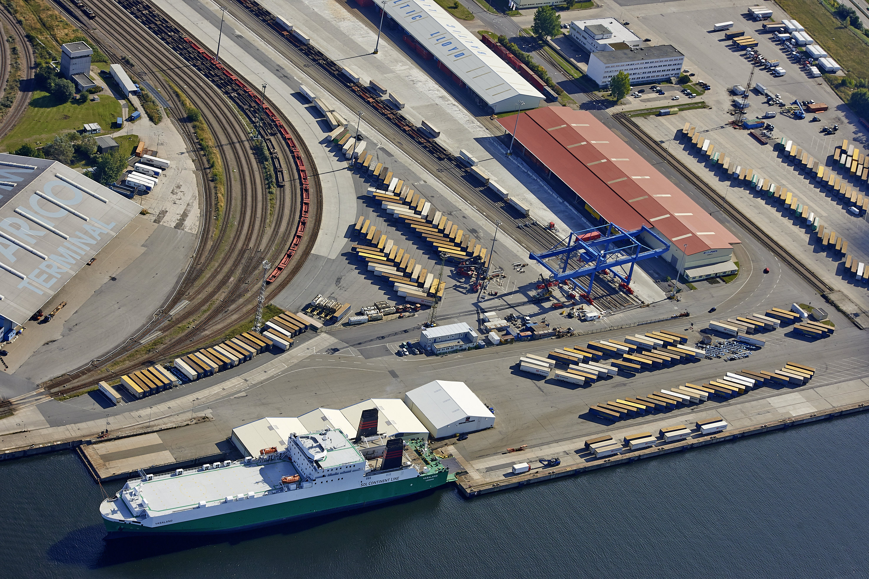 Aerial view of the intermodal terminal with railway tracks, truck trailers and a ferry berthed at the quay.