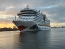 Das Kreuzfahrtschiff AIDAdiva läuft morgens bei Sonnenaufgang in den Hafen von Warnemünde ein, mit dem Rostocker Seehafen im Hintergrund.