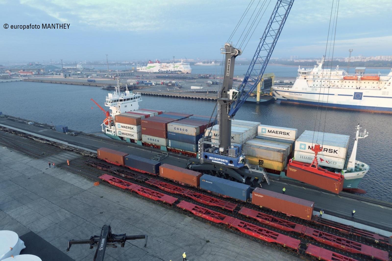 Ein Euroports-Hafenmobilkran verlädt von der Landseite aus einen Container auf ein Frachtschiff.