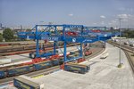 Zwei Portalkrane über Gleisanlagen mit Lkw-Walter-Aufliegern und Güterwaggons.