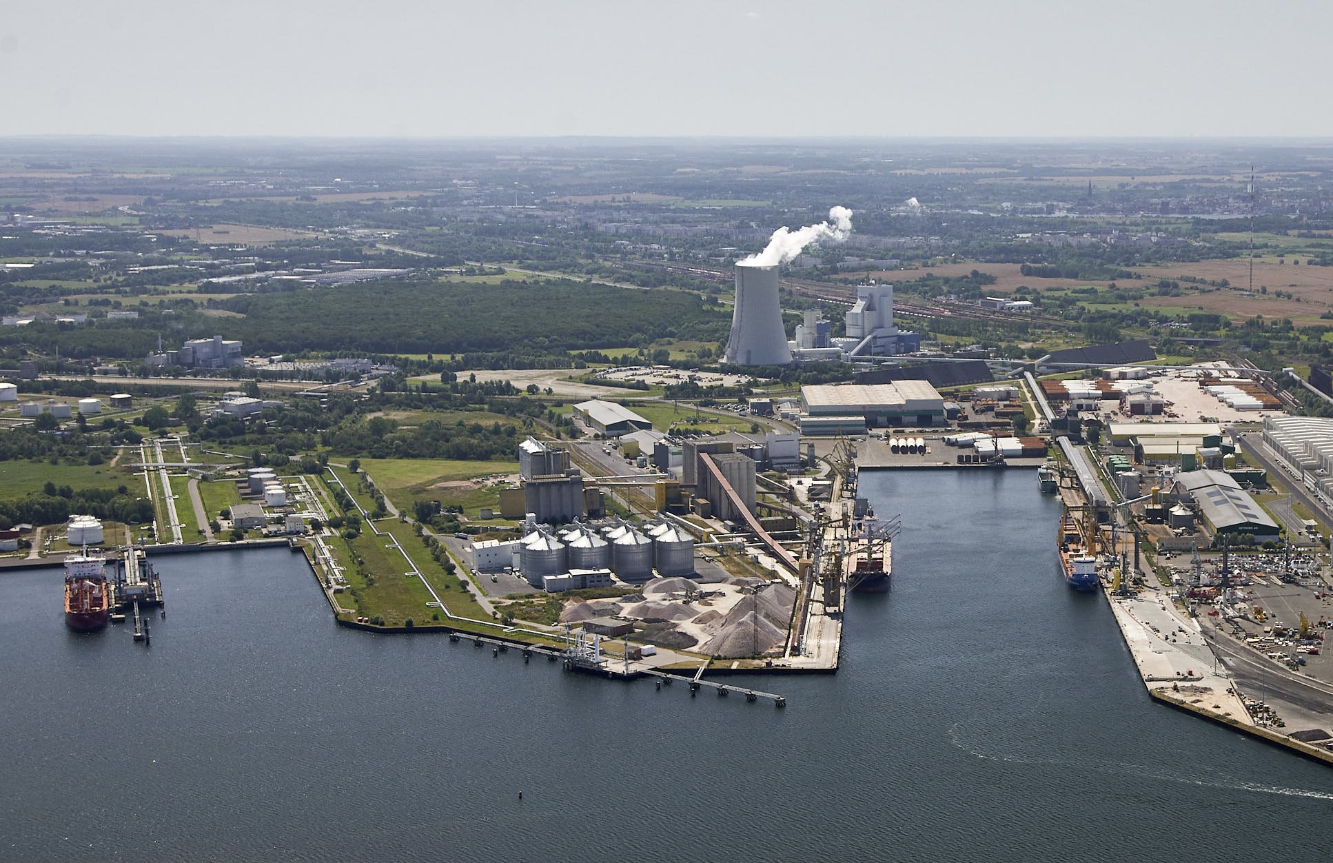 Luftaufnahme des Überseehafens Rostock mit Kaianlagen, Industrie- und Logistikflächen sowie Schiffen im Hafenbecken. 