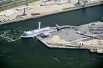 Luftaufnahme des Rostocker Fährhafens mit einer Scandlines Hybridfähre mit Rotorsegel im Vordergrund und weiteren Schiffen am Pier.