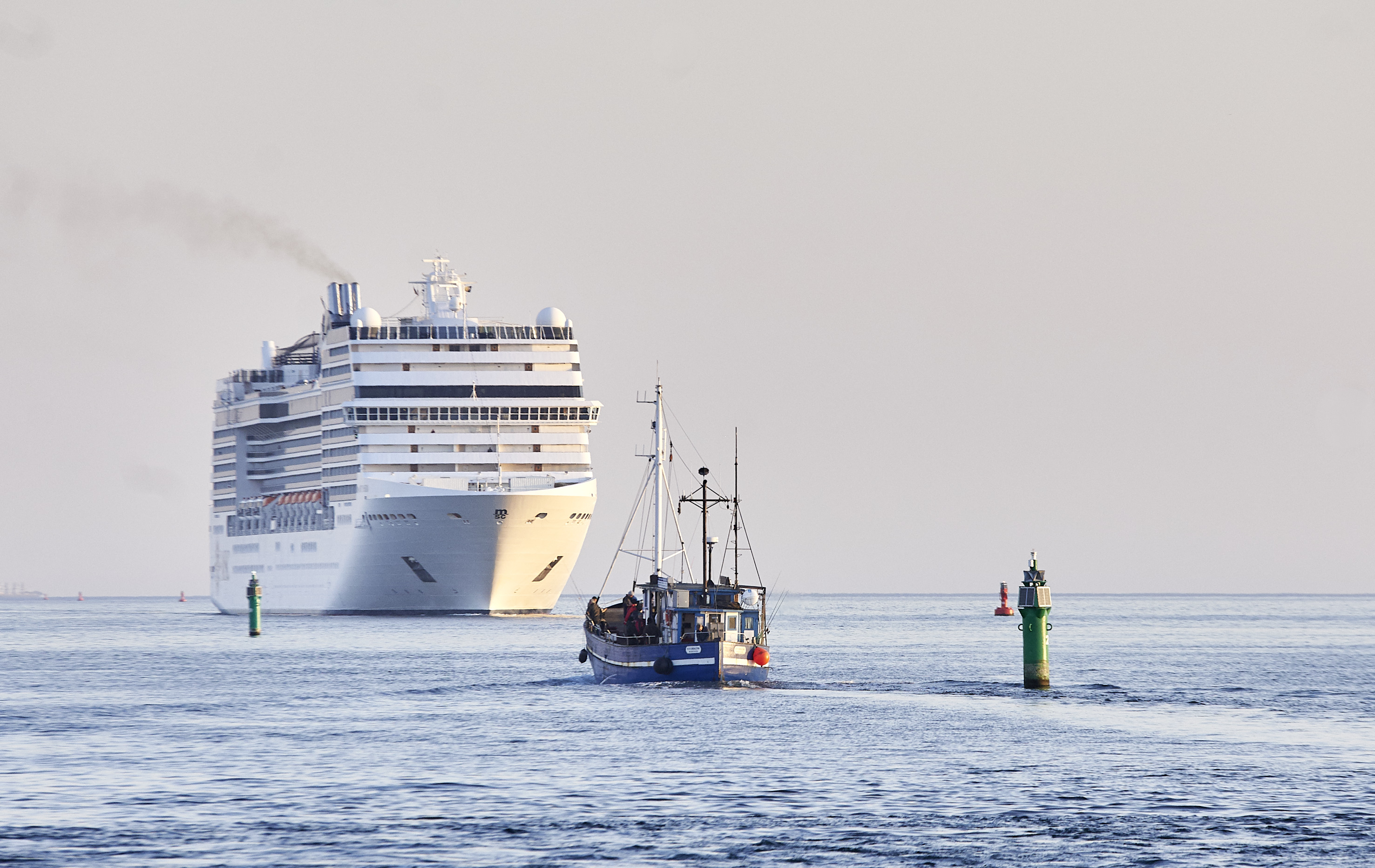Ein Fischkutter und ein Kreuzfahrtschiff begegnen sich bei der Ein- und Ausfahrt in den Hafen von Rostock.