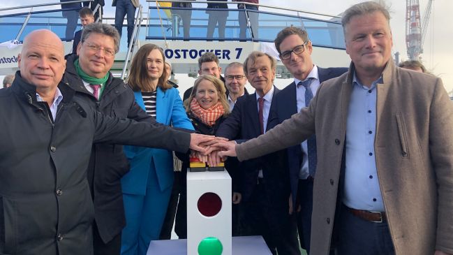 Sieben Personen drücken gleichzeitig einen Buzzer an Deck eines Fahrgastschiffes. Symbolischer Startschuss für den Baustart am Seekanal.